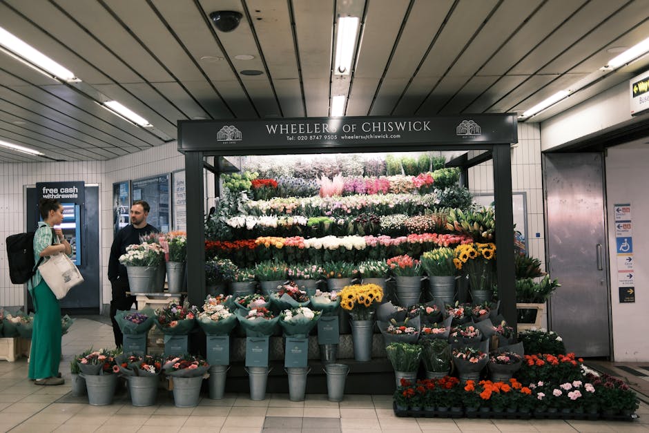 A vibrant display of fresh flowers arranged in a floral stand at Wheeler of Chiswick, situated within an underground station. The arrangement includes a variety of blooms such as white, pink, yellow,